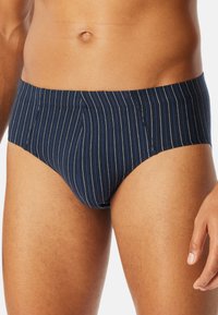 Caleçons de bain rayés navy en tissu extensible, avec des rayures verticales blanches, un ajustement serré et une taille basse.