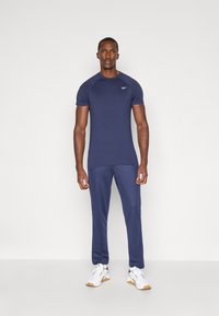 Ναυτικό αθλητικό μπλουζάκι κοντό μανίκι με ραφές στον λαιμό, συνδυασμένο με ταιριαστά κολάν, και τα δύο από μαλακό, ευέλικτο ύφασμα. Λευκά αθλητικά παπούτσια.