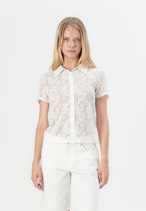 Short-sleeve, sheer white shirt with floral embroidery and a button-down collar. Paired with light-colored shorts.