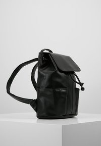 Černý kožený batoh s klopou, nastavitelnými popruhy, přední kapsou a hladkým povrchem. Navržen pro kompaktní rozměry.