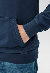 Felpa blu navy con polsini e orlo a costine, dotata di tasca a marsupio. Materiale morbido con una texture liscia.