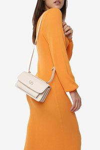 Hvid crossover-taske med klaplukning, guldfarvet hardware og tekstureret overflade, båret over en orange ribbet kjole.