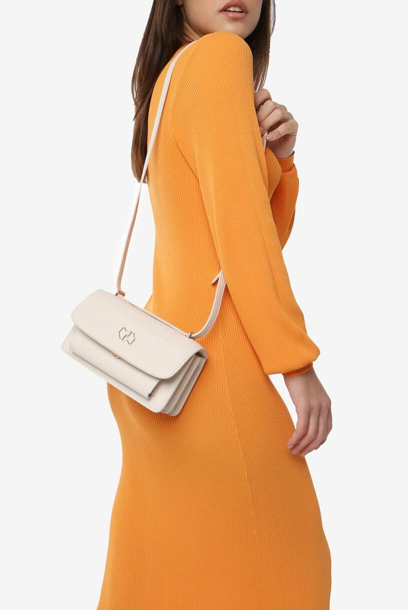 Hvid crossover-taske med klaplukning, guldfarvet hardware og tekstureret overflade, båret over en orange ribbet kjole.