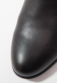 Zapato de cuero negro con una textura suave y brillante, diseño de punta redondeada y sutilezas en los detalles de costura a lo largo del borde.