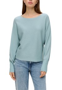 Hellblau gestreifter Pullover mit weitem Ausschnitt und langen Ärmeln, kombiniert mit hellblauen Jeans, die eine lockere Passform und weiche Textur zeigen.