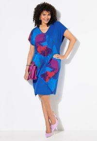 Modré šaty s barevným abstraktním vzorem v červené a fialové. Krátké rukávy a design s výstřihem do V. Spárováno s růžovými botami a odpovídající kabelkou.