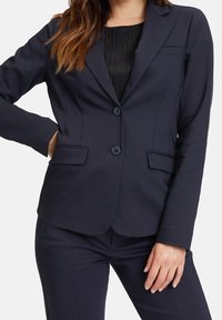 Marinblå skräddarsydd kavaj i slät tyg, med tvåknäppning, slagkrage och två framsydde fickor.