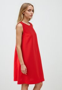 Abito rosso senza maniche realizzato in tessuto morbido, con scollo tondo e forma A-line ampia, con un orlo appena sopra il ginocchio.