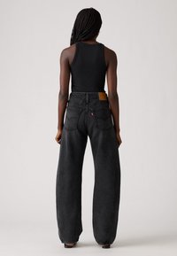 Vaqueros negros de pierna ancha con una cintura alta, que presentan un parche de cuero marrón y bolsillos traseros. Textura de mezclilla suave, corte recto.