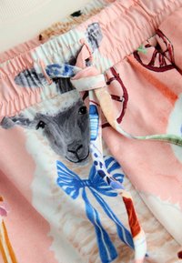 Różowe szorty z materiału z ilustracją owcy z niebieskimi akcentami, ściągaczem w pasie i gładką fakturą. Widoczne szczegóły wzoru ilustracyjnego.