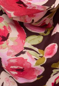 Tissu avec motif floral rouge et rose, feuilles vertes, et fond marron foncé, montrant des plis et des détails de texture.