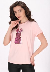 Světle růžové tričko s krátkým rukávem, které má design králíka se sekvínami v růžovém a černém leopardím vzoru. Měkká látka s kulatým výstřihem.