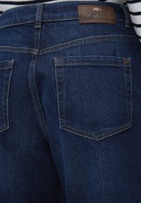 Σκούρο μπλε τζιν denim από πίσω, με δύο τσέπες και καφέ δερμάτινη ετικέτα με την επωνυμία "MOS MOSH" στη μέση.
