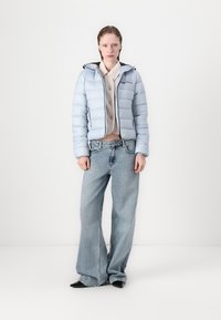 Lys blå puffjakke med sorte detaljer, kombinert med en beige genser og vide lys blå jeans. Sorte spisse sko fullfører antrekket.