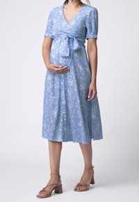Světle modré zavinovací šaty s krátkými rukávy, květinovým vzorem, páskem v pase a délkou po kolena. V kombinaci s béžovými sandály na block podpatku se středovými pásky.