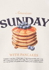 Un piccolo stack di pancake ricoperti di sciroppo e mirtilli, circondato da testo che mostra "Domenica Americana con pancake" e una breve ricetta per i pancake.