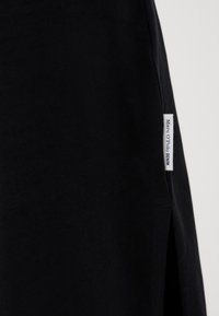 Black cotton fabric featuring a side slit and a small white branded label reading "Marc O’Polo DENIM." Smooth texture with minimal design.