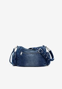 Sac à bandoulière en denim avec une forme courbée, doté d'un compartiment principal zippé, d'une poche zippée à l'avant et d'une bandoulière ajustable en bleu foncé.