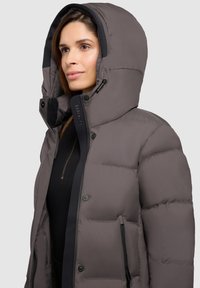 Puffy grey down jacket with a hood, featuring snap buttons, side zip pockets, and a black inner lining. Textured material with quilted pattern.