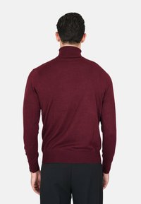 Maglione a collo alto bordeaux con maniche lunghe, colletto e orlo a coste. Texture morbida, design aderente e stile minimalista.