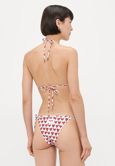 Bikini set featuring red heart patterns on a white background, halter neck ties, and adjustable side ties. Soft, lightweight fabric.