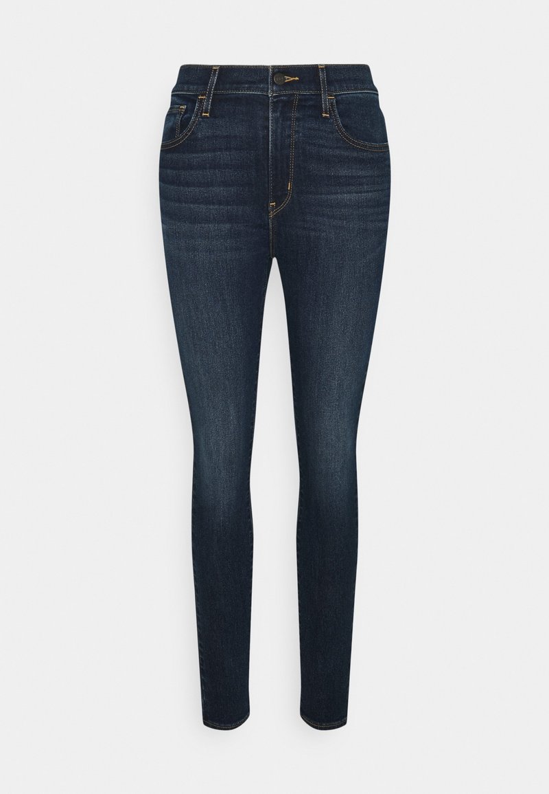 Jean skinny bleu foncé avec poches avant et arrière, fermeture à boutons et détails légèrement délavés sur les cuisses.