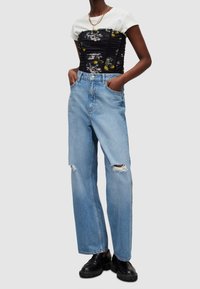 Corset noir à fleurs froncé porté sur un t-shirt blanc, associé à un jean en denim bleu clair taille haute avec genoux déchirés et des chaussures noires.