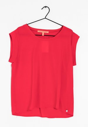 Czerwona bluzka z krótkim rękawem i okrągłym dekoltem zawieszona na czarnym wieszaku na białym tle.