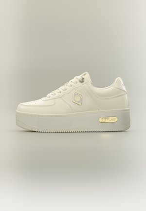Baskets en cuir blanc à plateforme basse avec lacets, badge logo doré sur le côté et plaque dorée sur la semelle, sur fond clair uni.