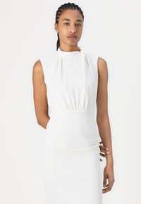 White sleeveless dress with a high neck, gathered waist, and smooth fabric. Simple, fitted design with a clean silhouette.
