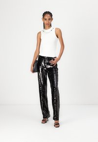 Top blanc sans manches avec un col rond, associé à un pantalon large noir pailleté. Accessoirisé avec un petit sac à main et des talons à lanières.