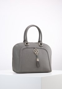 Borsa sintetica grigia con doppio manico, forma rotonda, chiusura con zip e un charm dorato con dettaglio in frangia. Texture liscia.