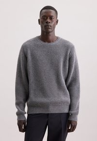 Maglione grigio a coste con collo rotondo, maniche lunghe e vestibilità rilassata. Modello con trama a maglia testurizzata, tessuto morbido, abbinato a pantaloni scuri.