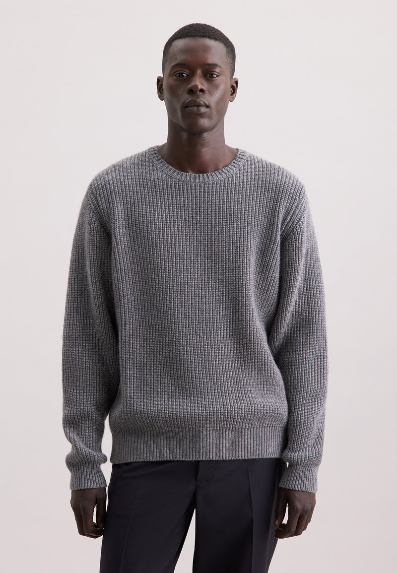 Maglione grigio a coste con collo rotondo, maniche lunghe e vestibilità rilassata. Modello con trama a maglia testurizzata, tessuto morbido, abbinato a pantaloni scuri.