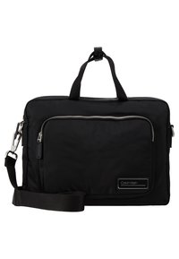 Serviette noire Calvin Klein avec poignées supérieures, poche avant zippée et bandoulière réglable avec attaches métalliques.