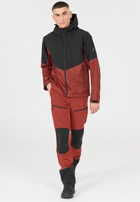 Röd och svart vattentät jacka med huva och dragkedjefickor, matchad med röda byxor med svarta detaljer och flera fickor.