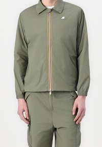 Olive green lightweight jacket with a collar, front zipper, and multi-colored stripe detailing along the zipper. Elastic cuffs.