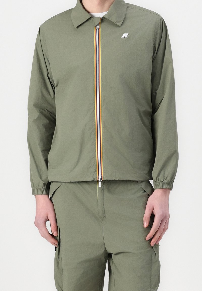 Olive green lightweight jacket with a collar, front zipper, and multi-colored stripe detailing along the zipper. Elastic cuffs.
