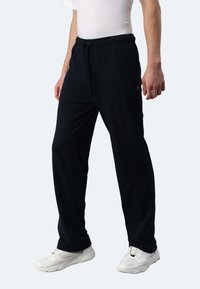 Navyblaue, elastische Hosen mit seitlichen Taschen, aus weichem Stoff, mit geradem Bein, kombiniert mit weißen Sneakers.