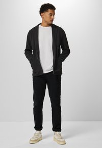 Mörkgrå sweatshirt med framfickor och huva, i kombination med en vit t-shirt och svarta byxor, kompletterad med beige sneakers.