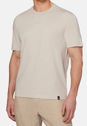 T-shirt beige à manches courtes en tissu doux ; présente un col rond et un petit logo imprimé sur la poitrine ; coupe décontractée.