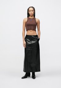 Καφέ κοντό τοπ με μικρό λογότυπο, σε συνδυασμό με μακριά μαύρη δερμάτινη φούστα. Το μοντέλο φοράει μαύρα μποτάκια με τακούνι. Λείες υφές και εφαρμοστά σχέδια.