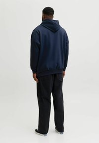 Sudadera con capucha navy de corte relajado, dobladillos acanalados y tela suave, combinada con pantalones sueltos negros y zapatillas casuales negras.