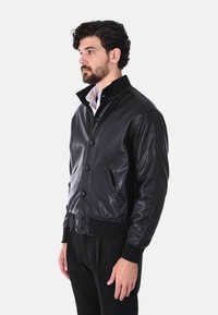 Giubbotto bomber in pelle nera con fondo a coste, chiusura a bottoni e due tasche laterali. Presenta un colletto a contrasto e una superficie liscia.