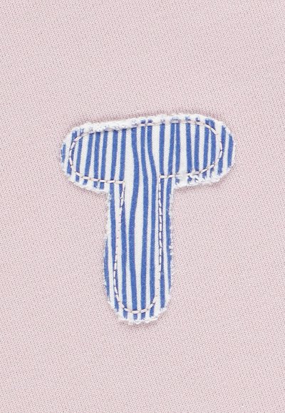 Sfondo di tessuto rosa con una patch a forma di "T" a righe blu e bianche, bordata da una cucitura bianca. La patch ha una finitura strutturata.
