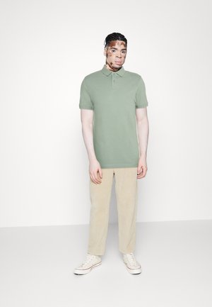 Grønn polo skjorte med korte ermer, kombinert med beige cordbuksler og hvite sneakers. Enkelt design, myk stoff, avslappet passform.