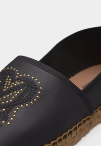 Μαύρο παπούτσι espadrille χωρίς κορδόνια με πλεκτή σόλα από τζούτ και χρυσές χάντρες σε κεντημένο πάνω μέρος.