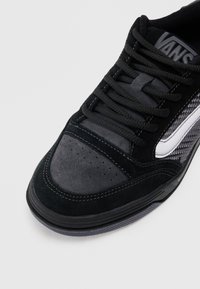 Sneaker nera in suede e tessuto testurizzato, con una striscia bianca a contrasto, punta rotonda e lacci neri con perforazioni sulla punta.