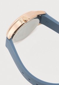 Rose gold watch case with crown and blue silicone strap shown from the side, highlighting the strap's texture and strap size marking.