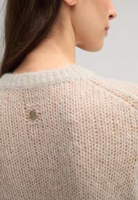 Leichter, gestrickter Pullover mit einer lockeren, luftigen Textur in Creme. Verfügt über ein kreisförmiges, metallisches Logodesign im Nackenbereich auf der Rückseite.